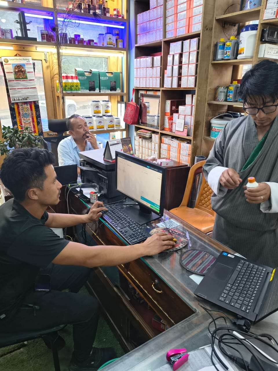Kezang Enterprise serving a customer on aBitPOS at the counter, surrounded by construction and hardware stock