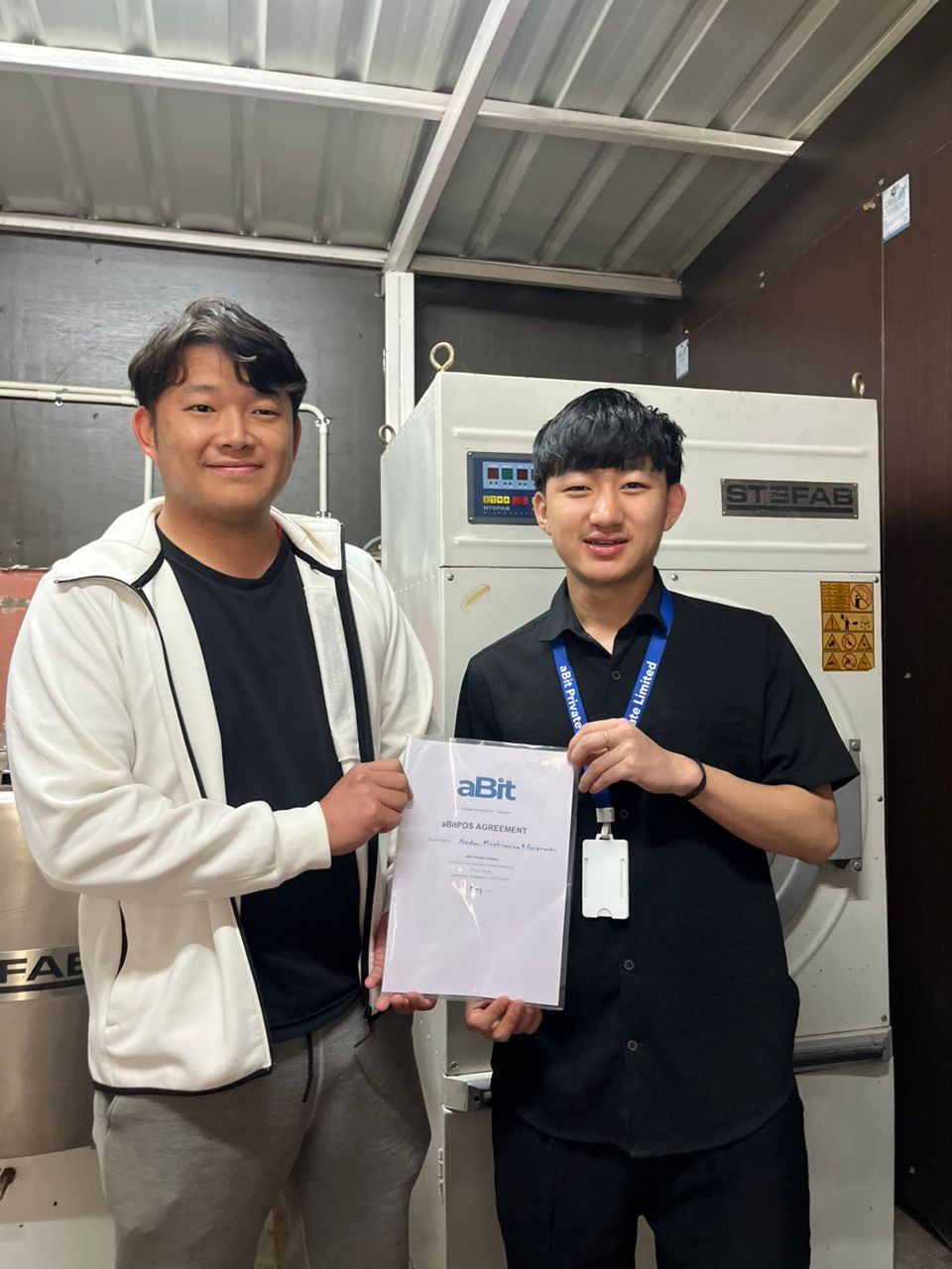 Norden Machineries representative with aBit team holding the signed aBitPOS agreement